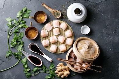 home made chinese and korean dumplings served on the traditional steamer and bamboo mat decorated with soy sauce, parsley, giner and green tea. top view