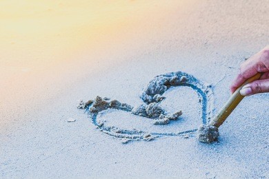 draw a heart on the sand to a loved one on valentine's day. the happy couple on sunset.