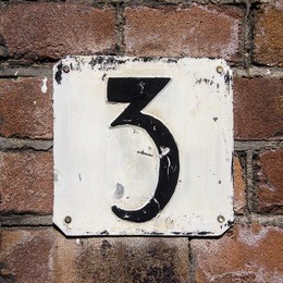 weathered and crackled house number three on a brick wall