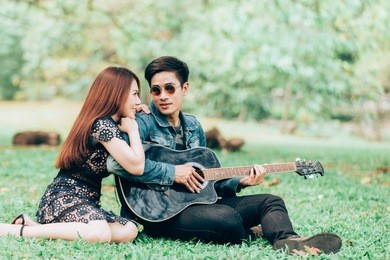asian couple in love playing acoustic song  guitar sitting on grass in the park