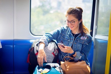 enjoying travel. young pretty woman with baggage traveling by the train or mass rapid transit(mrt) train near the window using smartphone. asian lady traveling commute train concept.