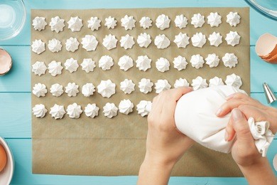female hands squeeze whipped cream on baking paper. step by step recipe of meringue cookies. process of meringue making top view.