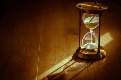sand running through the bulbs of an hourglass measuring the passing time in a countdown to a deadline, on a dark background with copy space. nostalgic tone.