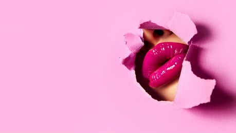 beautiful plump bright lips of pink color peep into the slit of colored paper.