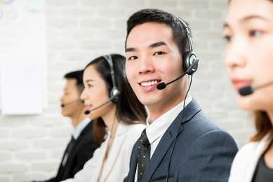smiling male asian customer service telemarketing agent working in call center with team