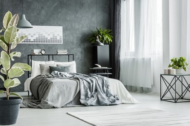 double bed with gray sheets near the window in monochromatic bedroom interior