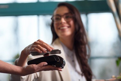 nfc technology. selective focus of mobile bank terminal hold by female hand and beautiful woman using nfc technology for making payment