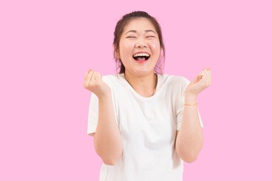 cute asian woman scream with joy and happiness, suprise feeling, winner expression, white shirt, pink background