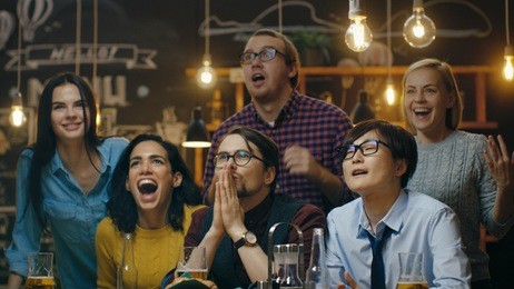 diverse group of friends watches tv in the sporstbar. their team scores the goal and wins. young people cheer.