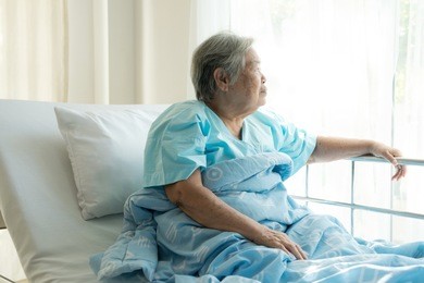 elderly patient alone in bed. alone and stress, missing her grand children. looking at window. very senior, old chinese woman.