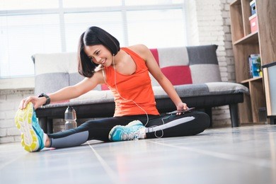asian women warm up before exercise at home and she's listening.