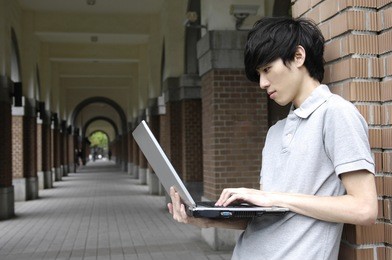 a handsome college student holding laptop on campus.