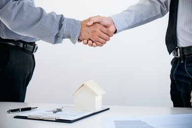 home loan insurance concept, broker agent shaking hands with customer after good deal agreement, home model.