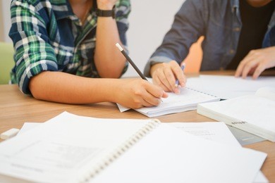 close up girl hand writing something and teaching her friend about calculus subject in library private room for test examination , education concept