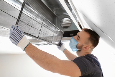 male technician cleaning industrial air conditioner indoors