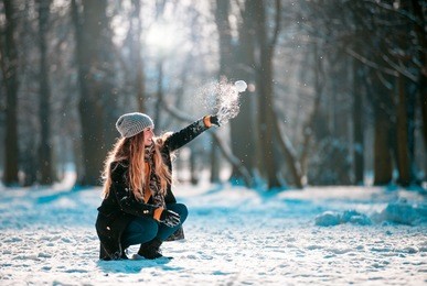 young woman throwing snowball at sunny day in the winter park