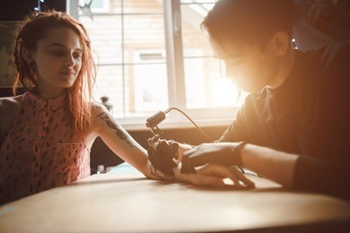 a tattoo artist makes a tattoo on the hand of a beautiful girl. concept art and tattoo