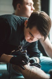 close up image of the tattoo male artist makes a tattoo on a female leg.