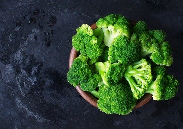 fresh raw broccoli in a wooden bowl on a dark background