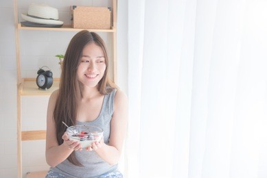 beautiful young asian woman eating yogurt with berries for breakfast in the morning