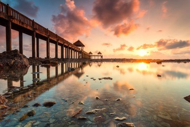 a long exposure picture of golden sunrise with stone jetty with reflection