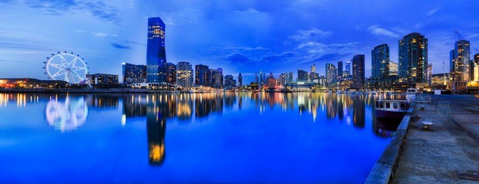 blue sunset panorama on docklands in melbourne when modern ubran achitecture reflects in still waters of yarra river.