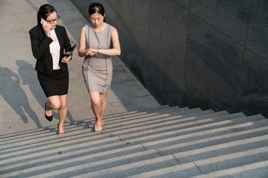 black suit office lady talking cellphone and the grey dress businesswoman looking at her watch. these two busy successful asian are going to train station and now waiting for someone.