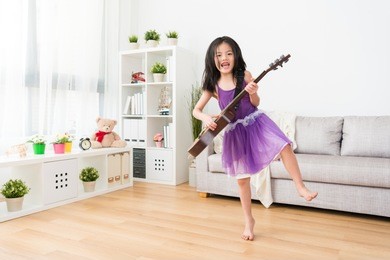 little asian girl raise up her leg and play the guitar music happily.