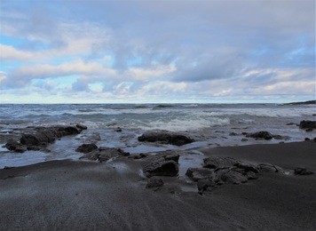 punalu'u black sand beach with calm waves, rocks, and cloudy blue sky, the big island, hawaii