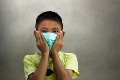 portrait of young boy, short hair, wearing yellow t-shirt, looking straight to camera, put his hand cover his mouth over mask to avoid infection from flu, diseases or pollution that spread in the air.