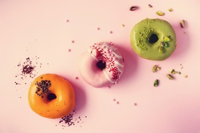 colorful donuts with icing on pastel pink background. sweet orange, green, pink doughnuts with pistachio, chocolate. flat lay, top view, copy space.
