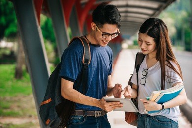 a group of young or teen asian student in university smiling and reading the book and look at the tablet or laptop computer in summer holiday.