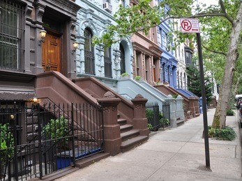 brownstone homes tree lined urban street with no parking street cleaning sign on sidewalk manhattan new york city