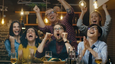 diverse group of friends watches tv in the sporstbar. beautiful young people drink, have fun and cheer for their team.