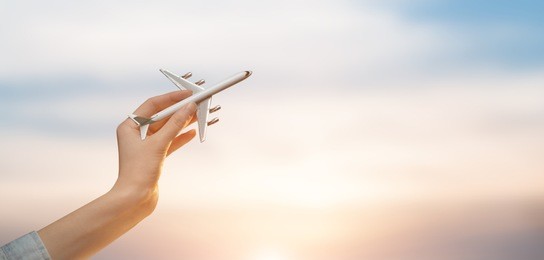 woman holding airplane in hands and flying over the sunset background