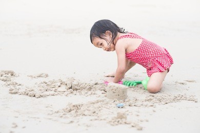 attractive adorable asian little girl is wearing red swimming suit and playing sand on the beach with happiness moment, concept of happy and healthy kid lifestyle and learning by playing activity.