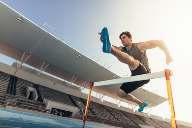 close up of a runner jumping over an hurdle during track and field event. athlete running a hurdle race in a stadium.