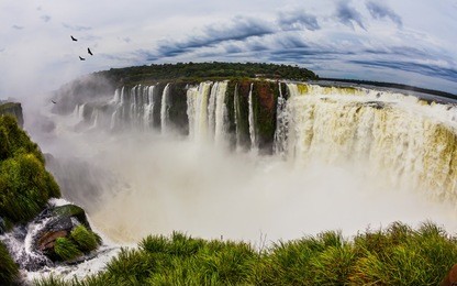 andean condors fly above the roaring iguazu waterfall. grandiose waterfalls iguazu in the rainy season - the devil's throat. concept of active and photographic tourism