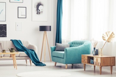 wooden cupboard next to blue armchair in cozy living room interior with beige settee