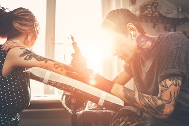 a young guy, beats a tattoo on the hand of the girl in a tattoo parlor, rotary tattoo machine, black ink, lens flare
