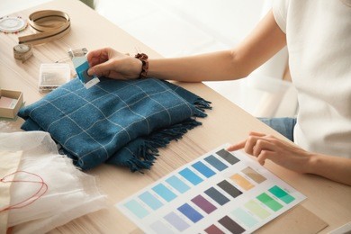 female fashion designer holding color samples choosing fabric textile blue shades at workplace, dressmaker or tailor working at desk pointing at set palette making choice selection, close up view