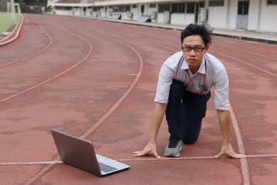 confident young asian businessman with laptop ready start position to forward on race track. business vision concept.