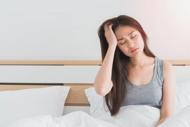 young asian woman feel headaches and discomfort on bed in white bedroom morning.concept of women's health care.