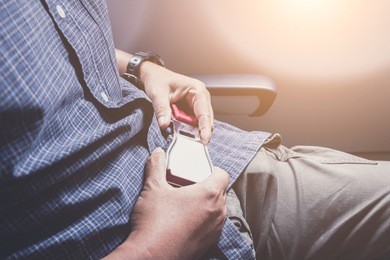 close up of man hands fasten belts while sitting on airplane seat.