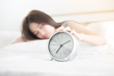 closeup alarm clock in the morning, wake up time , woman sleep on white bed, she feel lazy, woman push alarm clock in the morning