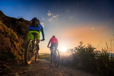 mountain biking women and man riding on bikes at sunset mountains forest landscape. couple cycling mtb enduro flow trail track. outdoor sport activity.