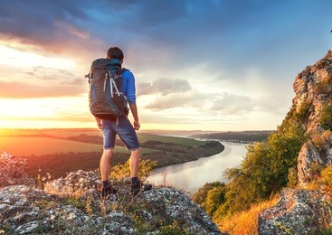 man with backpack on a top of rock ower beautiful canyon river landscape. travel hiker looking away.
