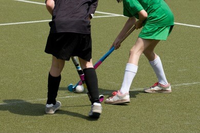 two girls play field hockey on artificial grass field