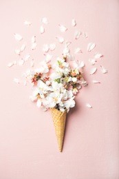 flat-lay of waffle sweet cone with white almond blossom flowers over pastel light pink background, top view. spring or summer mood concept