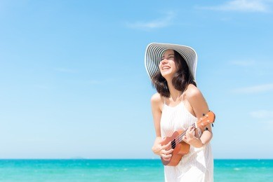 summer vacation. smelling asian women relaxing and playing an ukulele on the beach, so happy and luxury in holiday summer, blue sky background. travel and lifestyle concept.